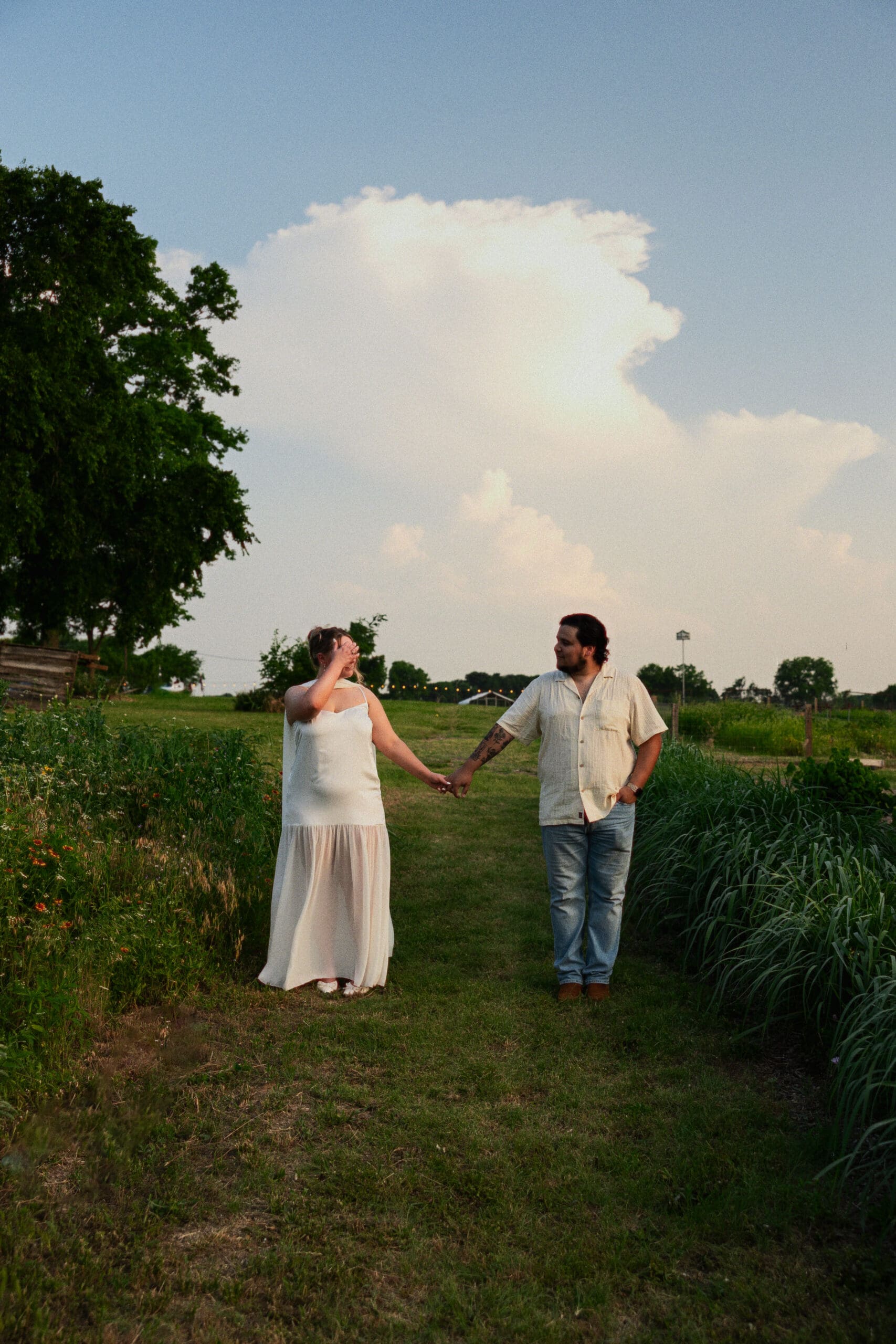 An engaged couple holding hands in a countryside field